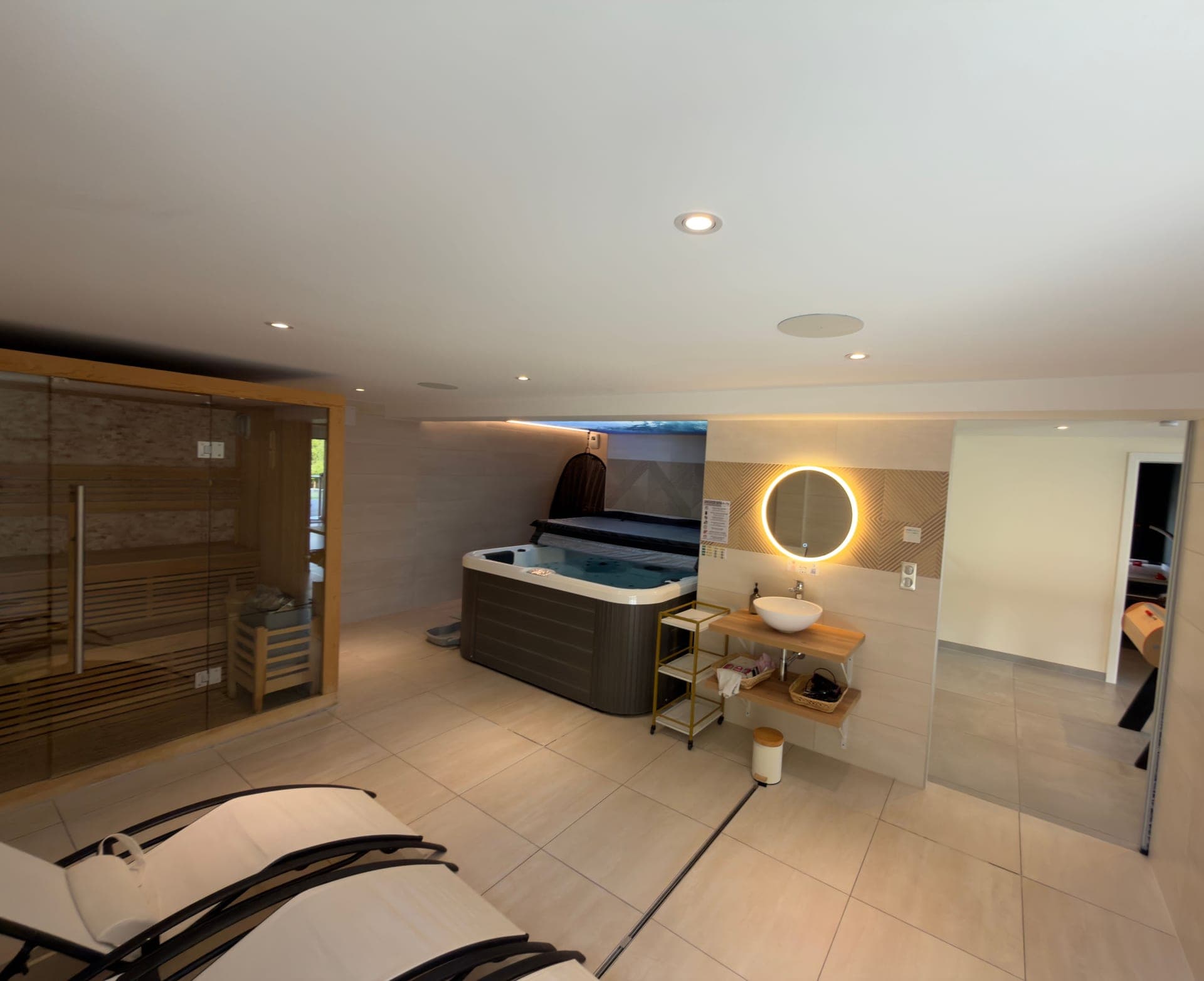 Vue large de l’espace bien-être à Dettwiller, sauna vitré, jacuzzi, miroir rond, chambre en enfilade