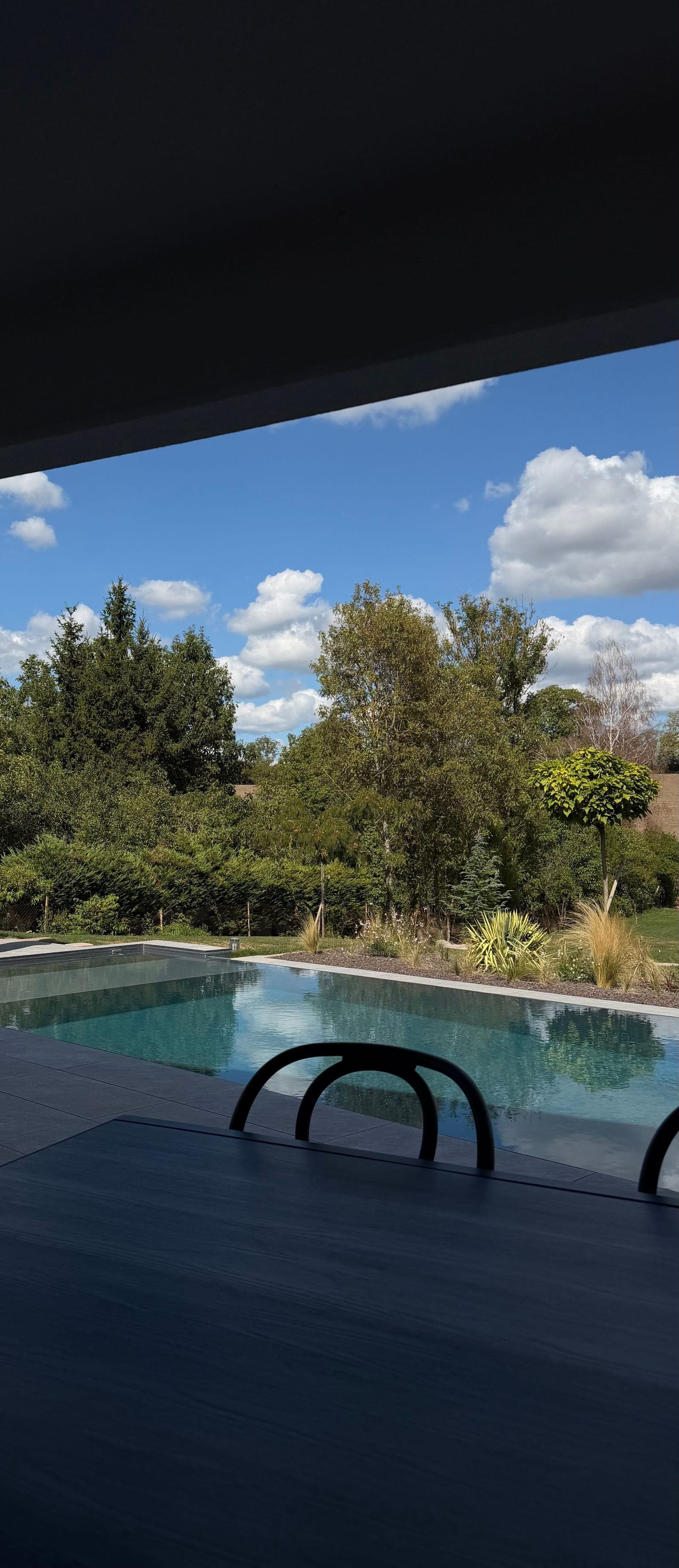 Piscine à débordement et jardin arboré cadrés par la terrasse couverte, ciel nuageux, villa à Dettwiller