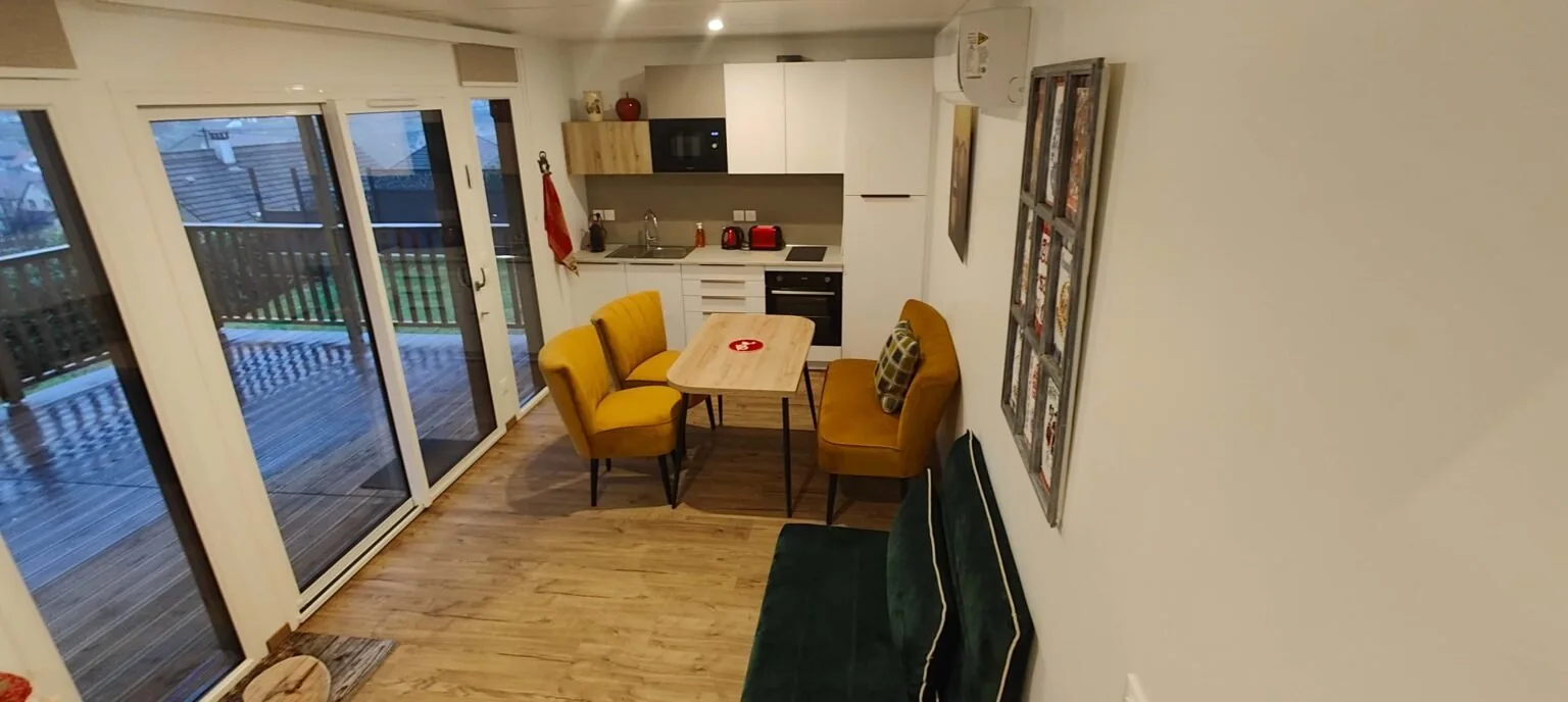 Séjour et cuisine du chalet Aux Sons des Cloches, avec fauteuils jaunes et accès à la terrasse