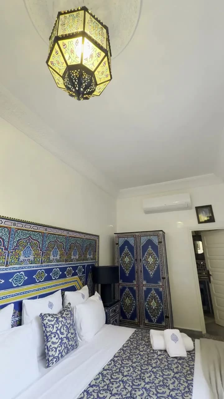 Chambre du Riad O’Zeen avec armoire peinte en bleu, motifs muraux et lanterne suspendue